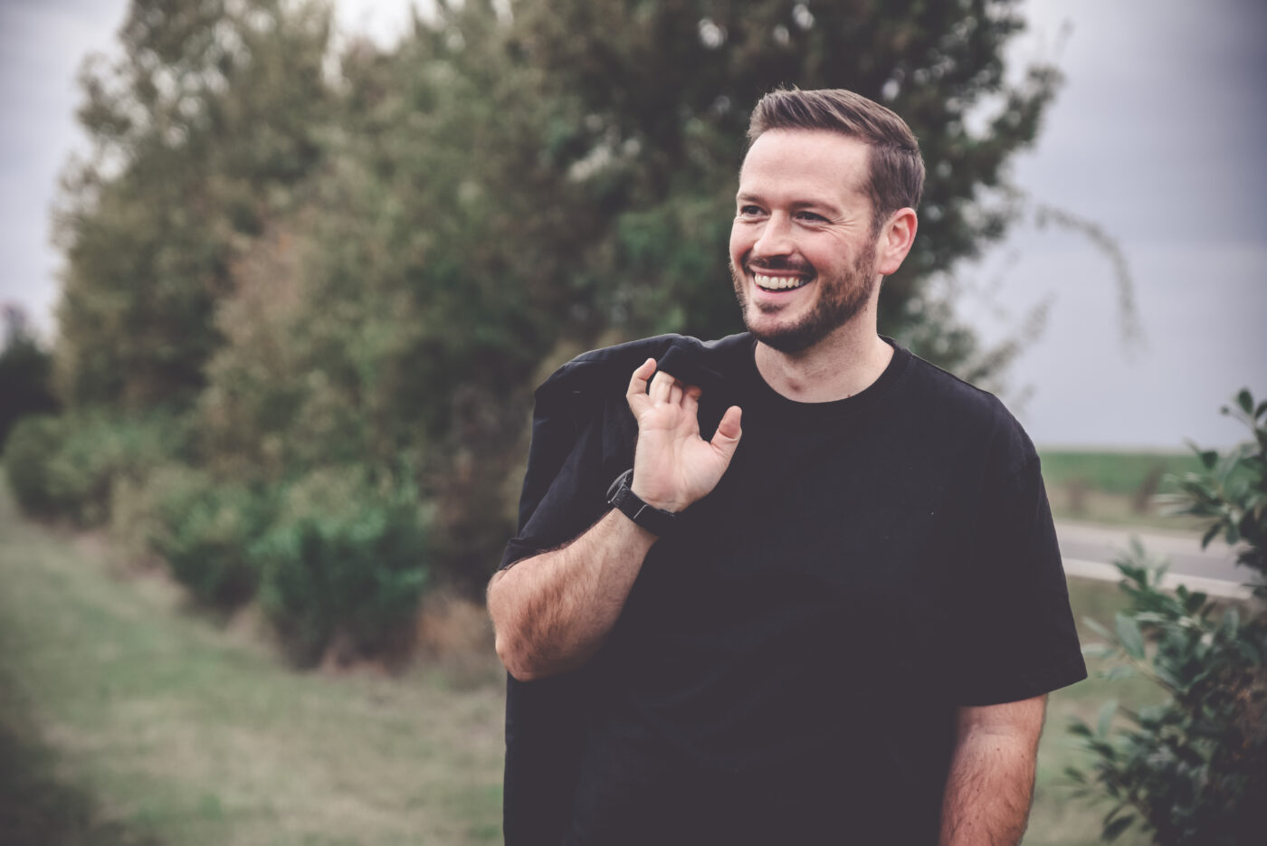 Benjamin Schäfer lächelt entspannt im Freien, eine schwarze Jacke locker über der Schulter tragend.